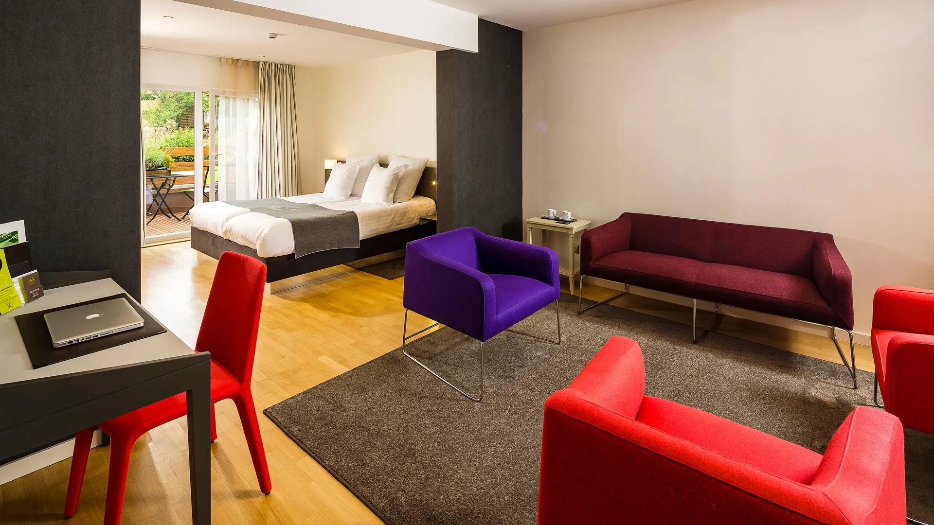 Chambre avec lit, canapé, fauteuils, table avec ordinateur portable et vue sur un balcon