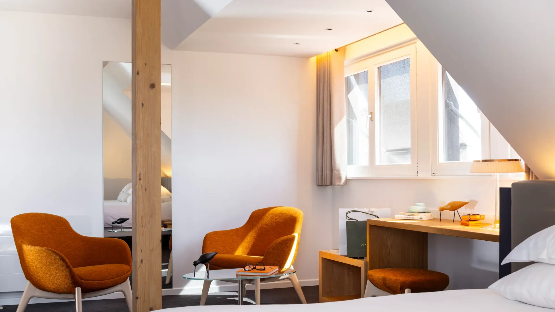Room with bed, desk, two orange armchairs and a coffee table near a window