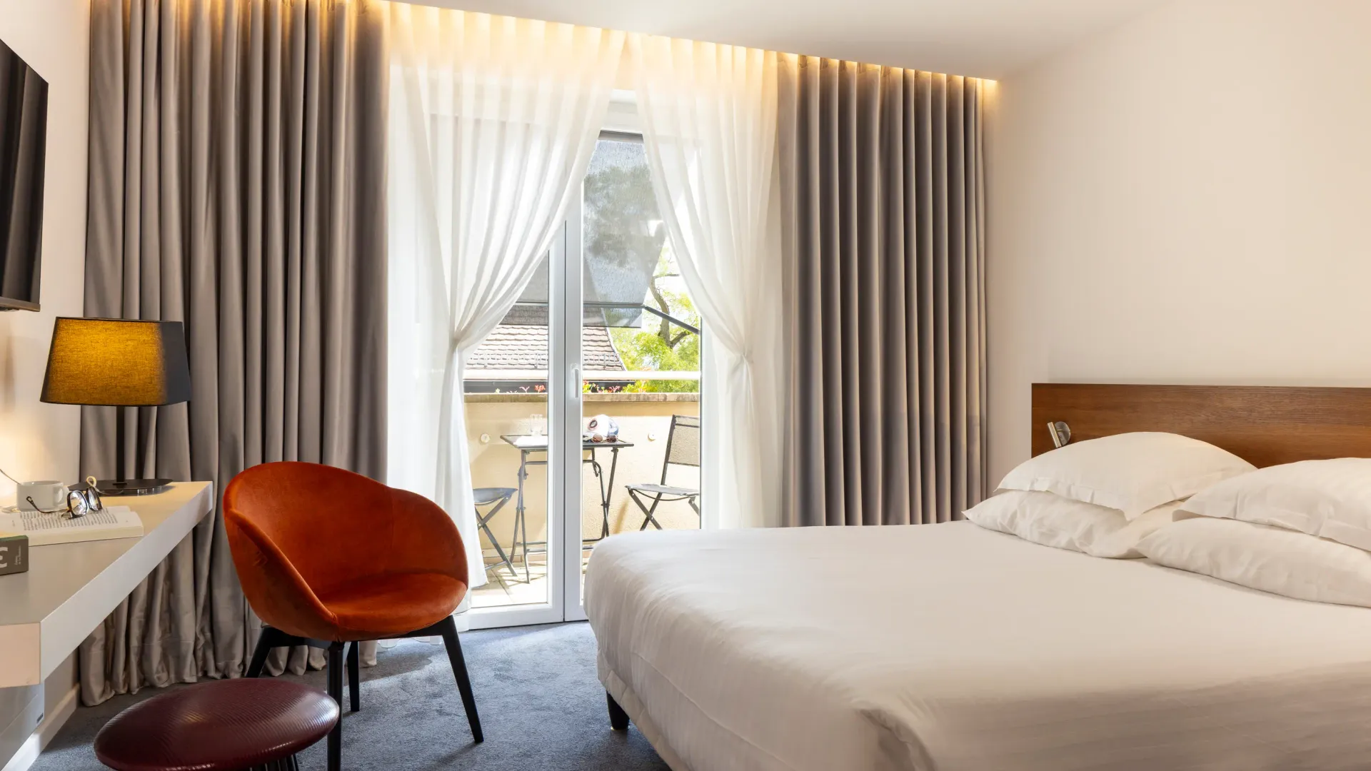 Room with a double bed, a bedside table, a lamp, a leather armchair, and a French window opening onto a balcony.