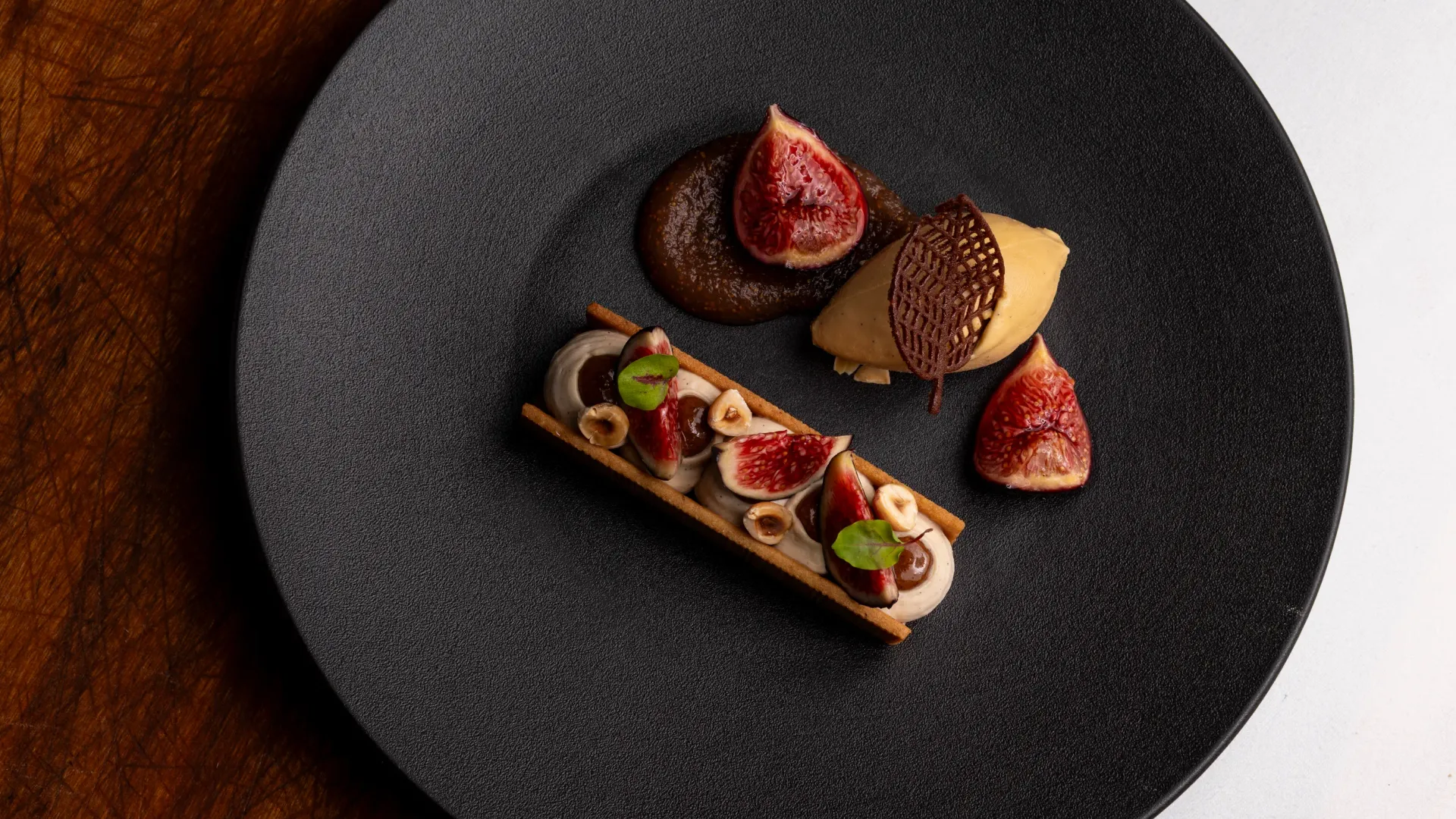 Assiette noire avec des figues, des garnitures et une fine tranche de pain sur une table en bois